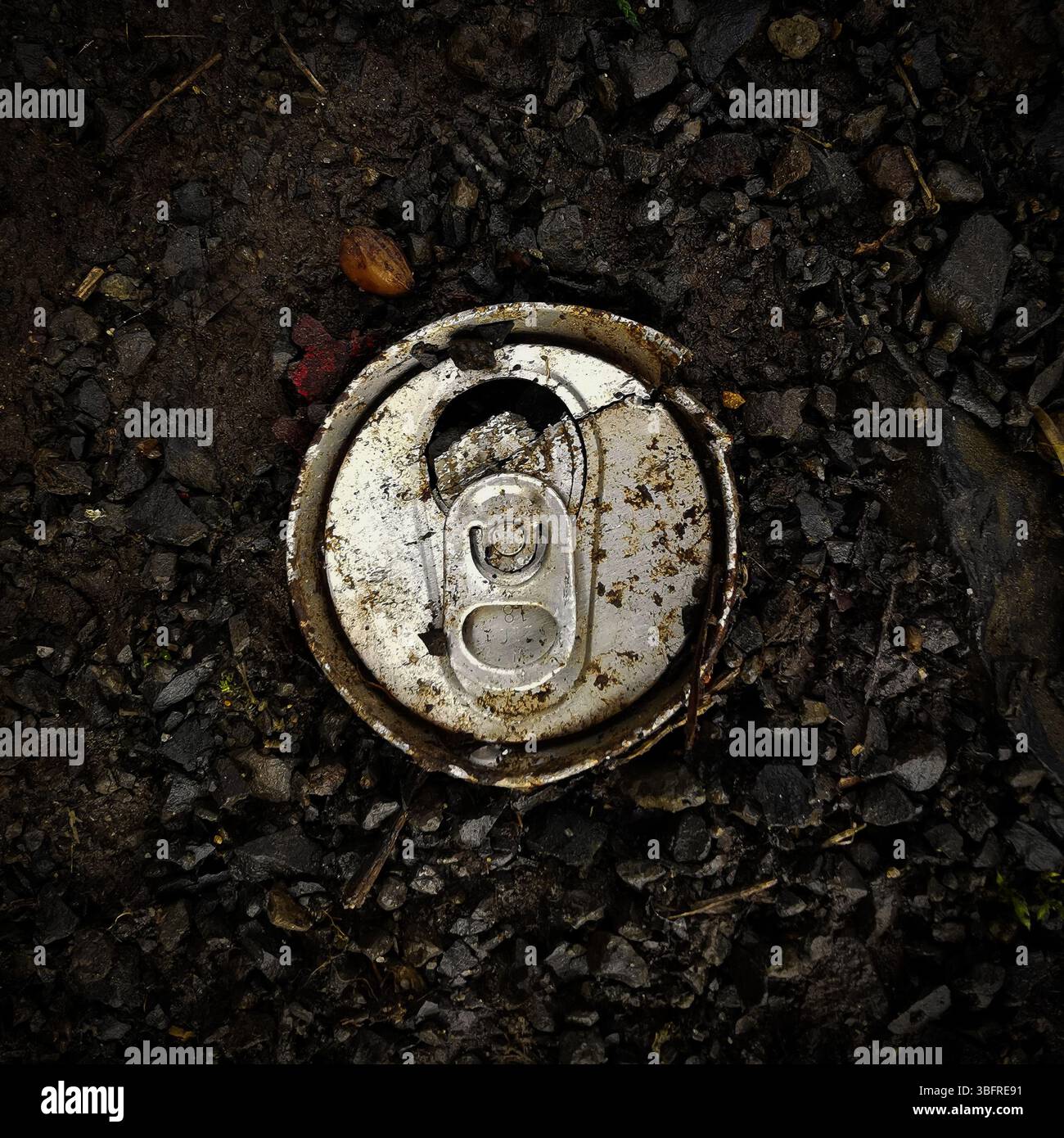 Una lattina di alluminio si trova abbandonata su un terreno scuro e ricco intervallato da piccoli ciottoli, sottolineando il problema dei rifiuti negli ambienti esterni Foto Stock