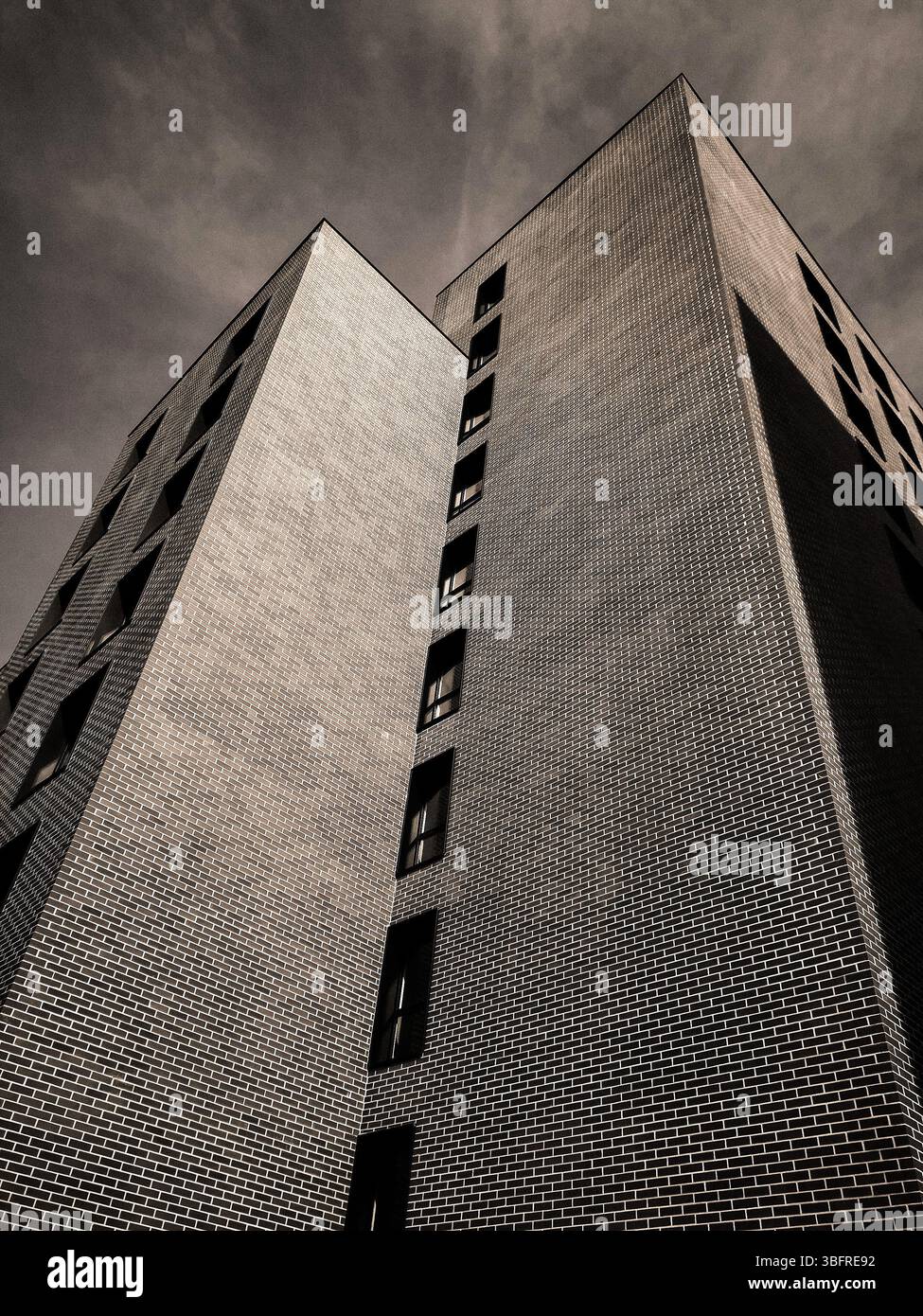 Un edificio suggestivo presenta forme geometriche uniche e intricati lavori in mattoni, torreggianti in alto contro un cielo umido in un ambiente urbano contemporaneo. Foto Stock