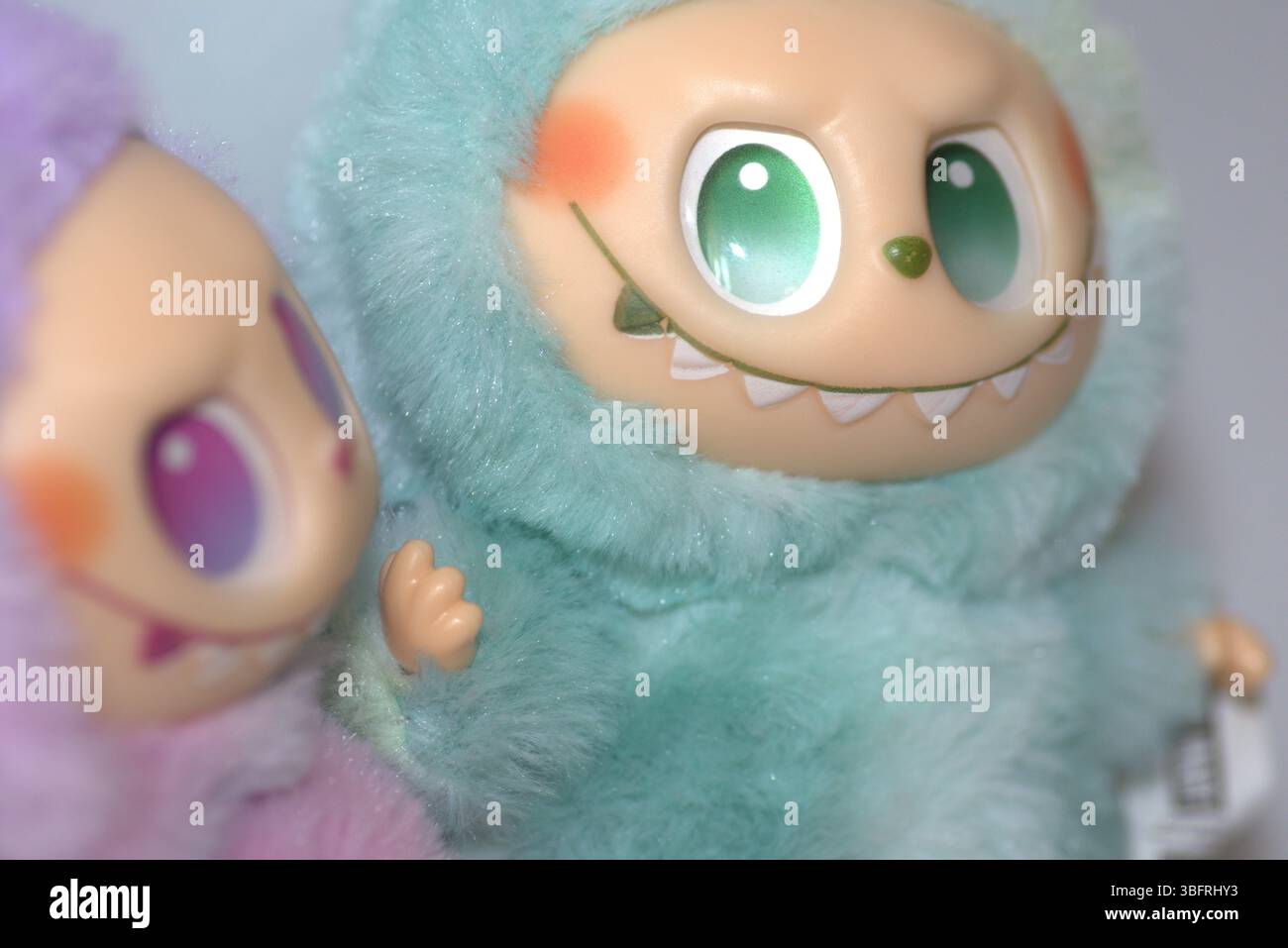 Due giocose figure di giocattoli Labubu in morbidi costumi da mostro verde e rosa e un sorriso malizioso, posate su uno sfondo bianco. Foto Stock