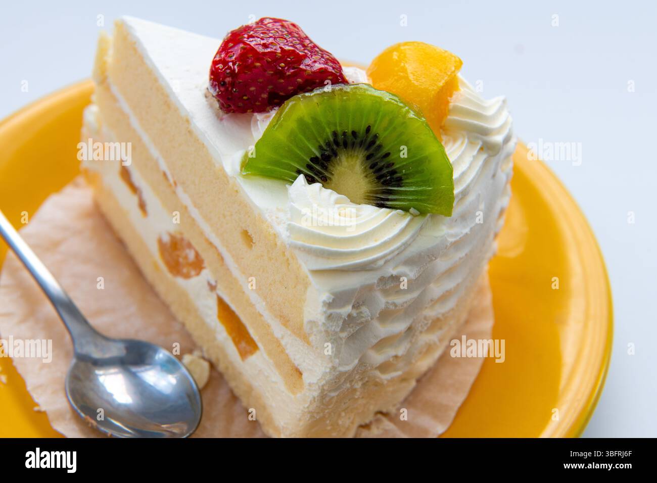 Primo piano di una fetta di torta alla frutta con fragole, pesca e kiwi isolati su bianco. Foto Stock