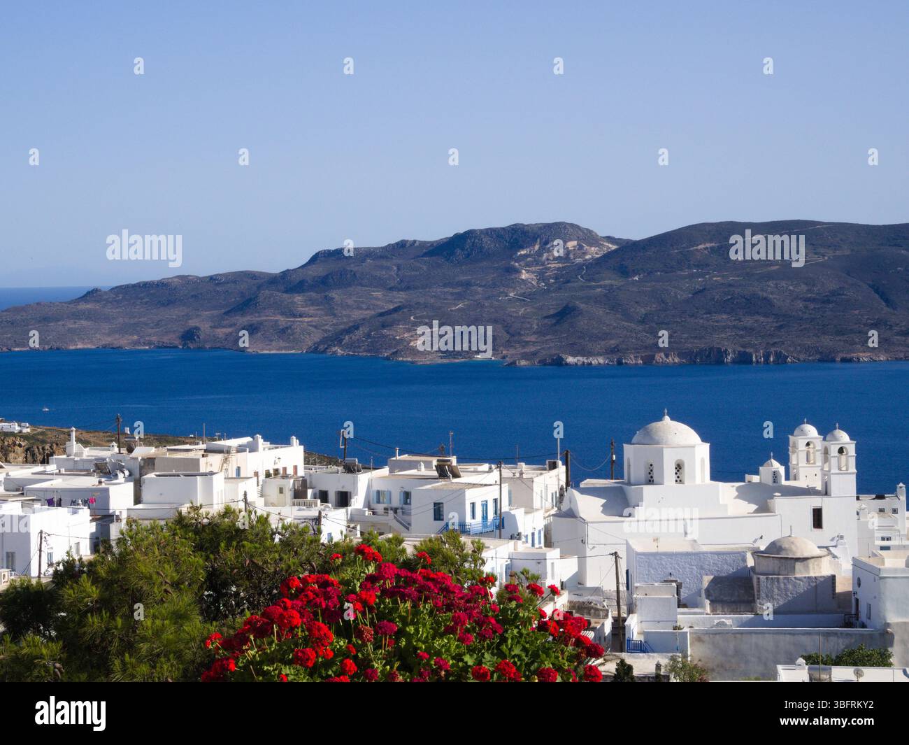 Vista panoramica di Plaka sull'isola di Milos, Cicladi, con architettura bianca, gerani rosa, Mar Egeo, e la baia di montagna. Solo per uso editoriale. Foto Stock