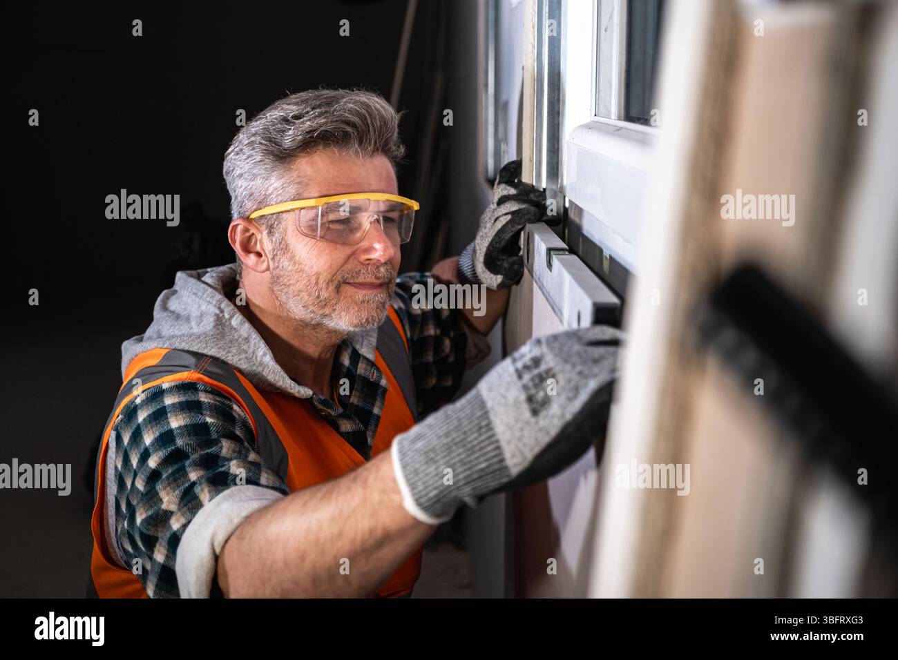 Primo piano di un lavoratore qualificato che utilizza una livella a bolla d'aria per garantire un preciso allineamento orizzontale di una finestra appena installata in un cantiere edile Foto Stock