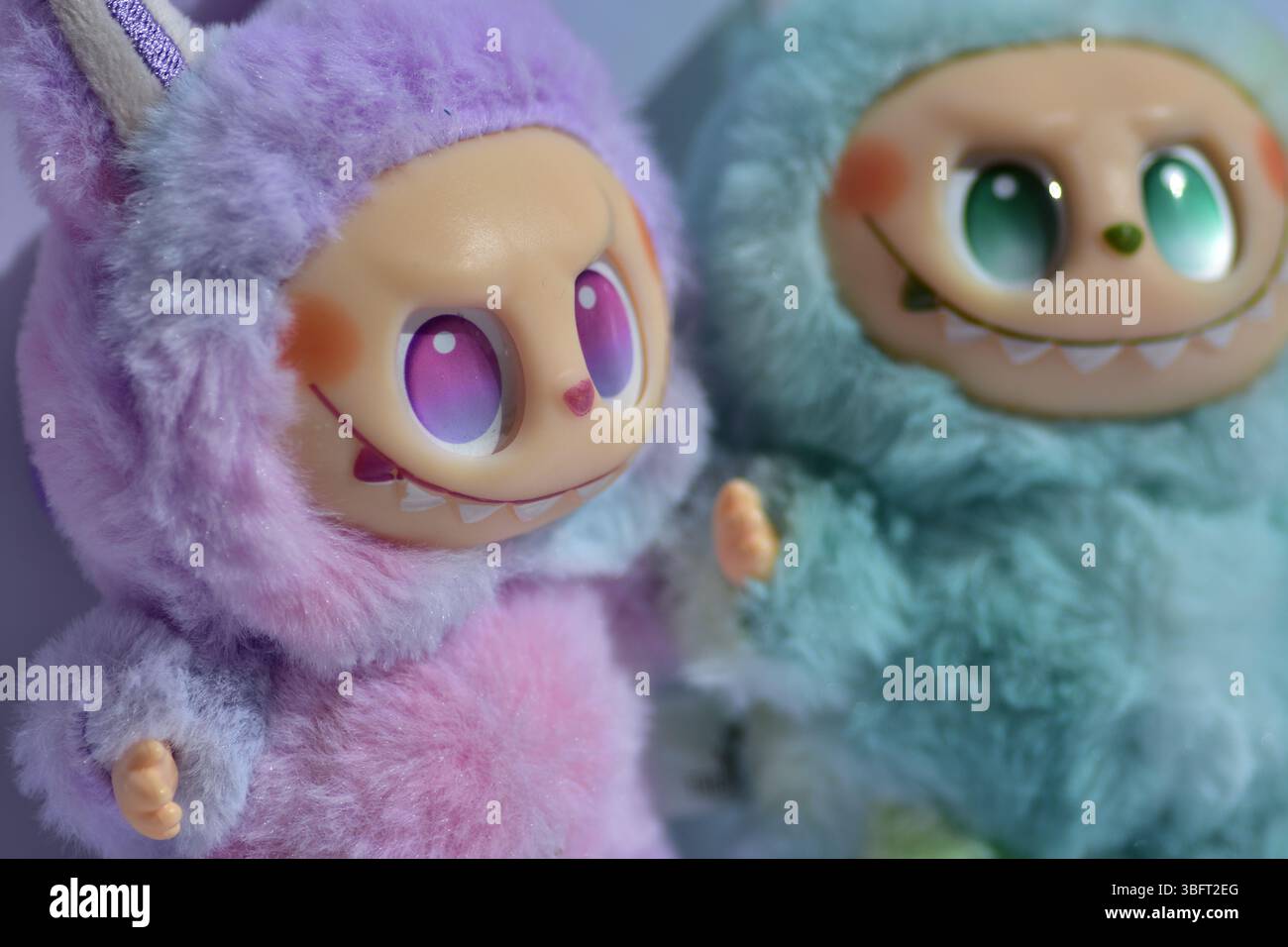Due giocose figure di giocattoli Labubu in morbidi costumi da mostro blu e rosa e un sorriso malizioso, posate su uno sfondo bianco. Foto Stock