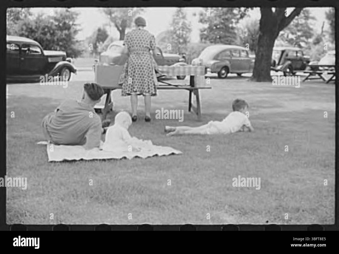 Un gruppo di picnic che si godono una giornata all'aperto, probabilmente in un parco o in uno spazio pubblico, con cibo e posti a sedere visibili. La scena cattura le persone che si impegnano in un incontro informale all'aperto, tipico delle uscite sociali durante il tempo più caldo. Foto Stock Un gruppo di picnic che si godono una giornata all'aperto, probabilmente in un parco o in uno spazio pubblico, con cibo e posti a sedere visibili. La scena cattura le persone che si impegnano in un incontro informale all'aperto, tipico delle uscite sociali durante il tempo più caldo. Foto Stock