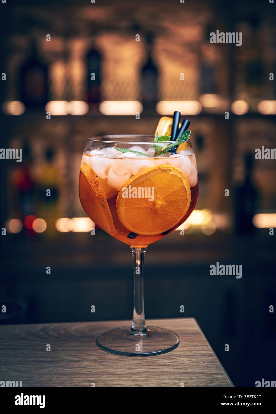 Un cocktail arancione con ghiaccio e menta in un bicchiere di vino è seduto su un bancone del bar Foto Stock Un cocktail arancione con ghiaccio e menta in un bicchiere di vino è seduto su un bancone del bar Foto Stock