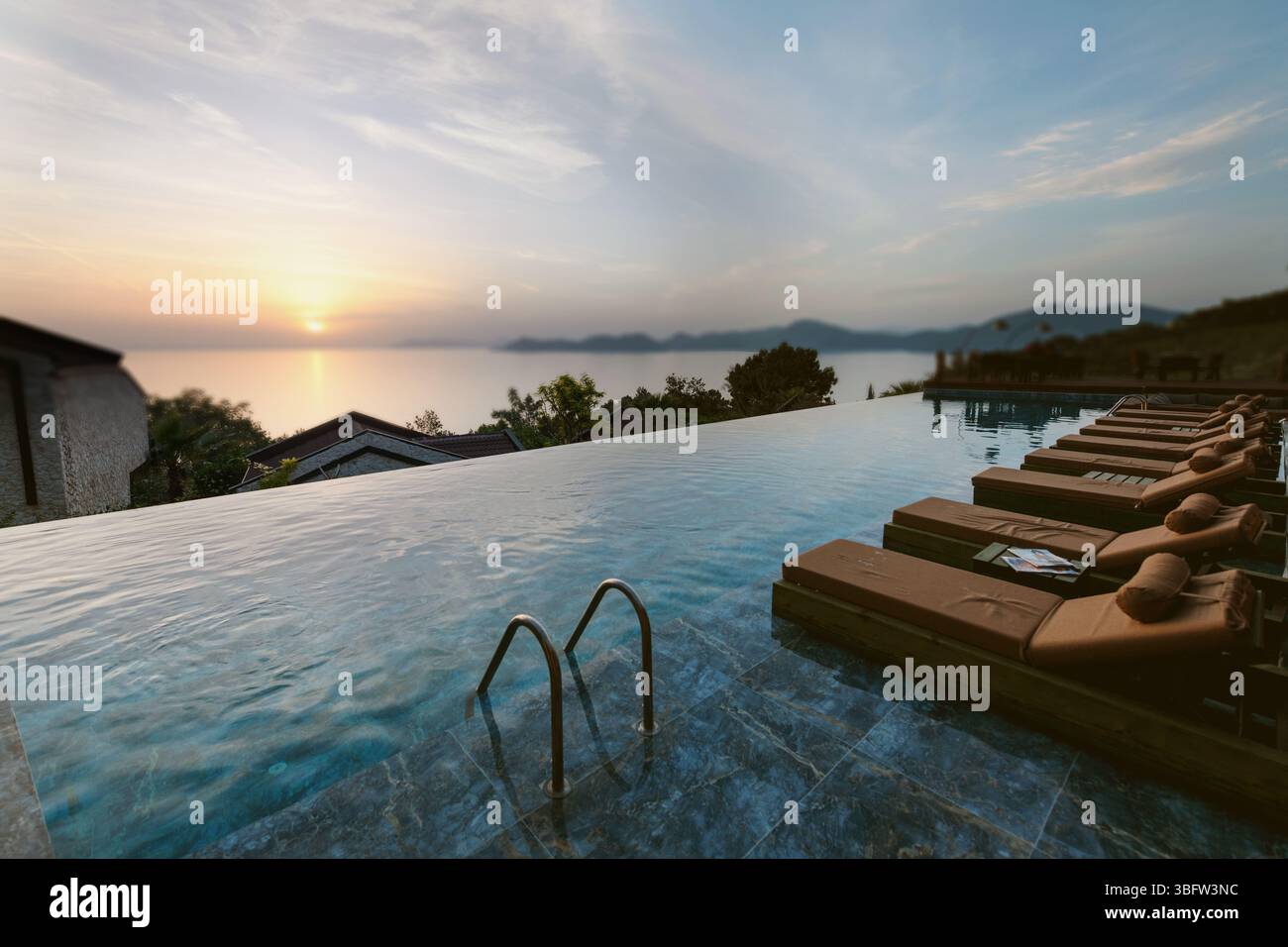 Un invitante lettino siede vuoto accanto a una piscina a sfioro, inondato dalla luce dorata del tramonto e con vista infinita sull'oceano. Foto Stock