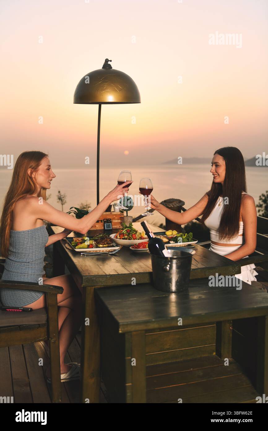 Due donne brindano con gioia con bicchieri da vino a un elegante tavolo da pranzo durante una serata speciale. Foto Stock