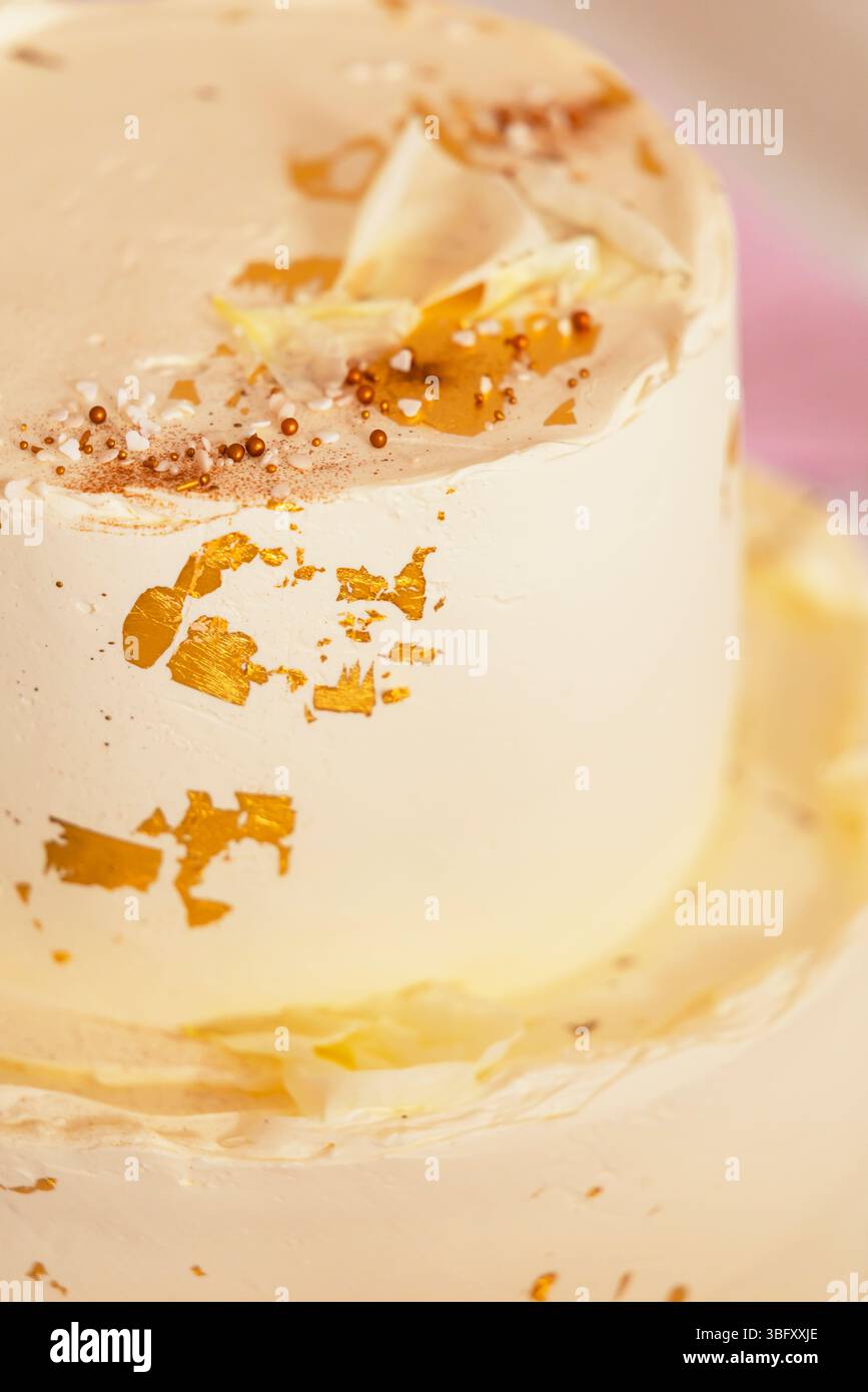 Torta cremosa a due livelli decorata con foglie d'oro, scaglie di cioccolato bianco e sprinkles, perfetta per i festeggiamenti Foto Stock