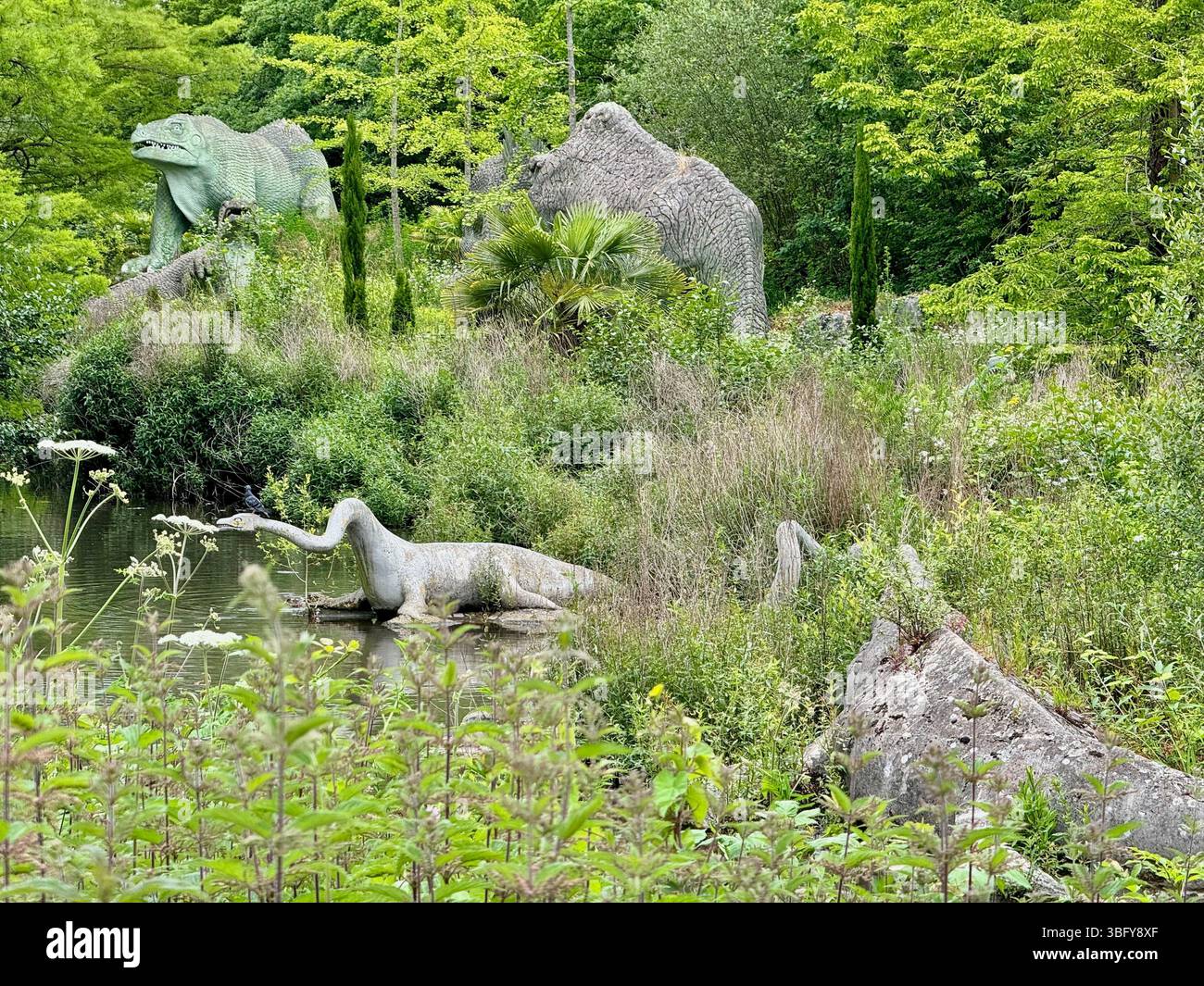 Londra, Inghilterra - 9 giugno 2024: Sculture di dinosauri preistorici annidate nel verde lussureggiante del Crystal Palace Park. - Immagine stock catturata con smartphone
