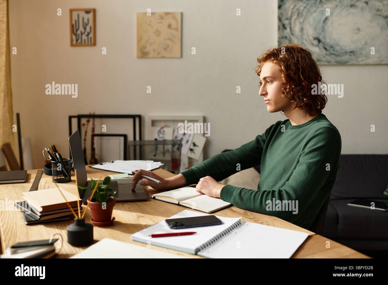 Un giovane attento si impegna in un lavoro creativo nel suo elegante spazio di lavoro domestico pieno di calore Foto Stock