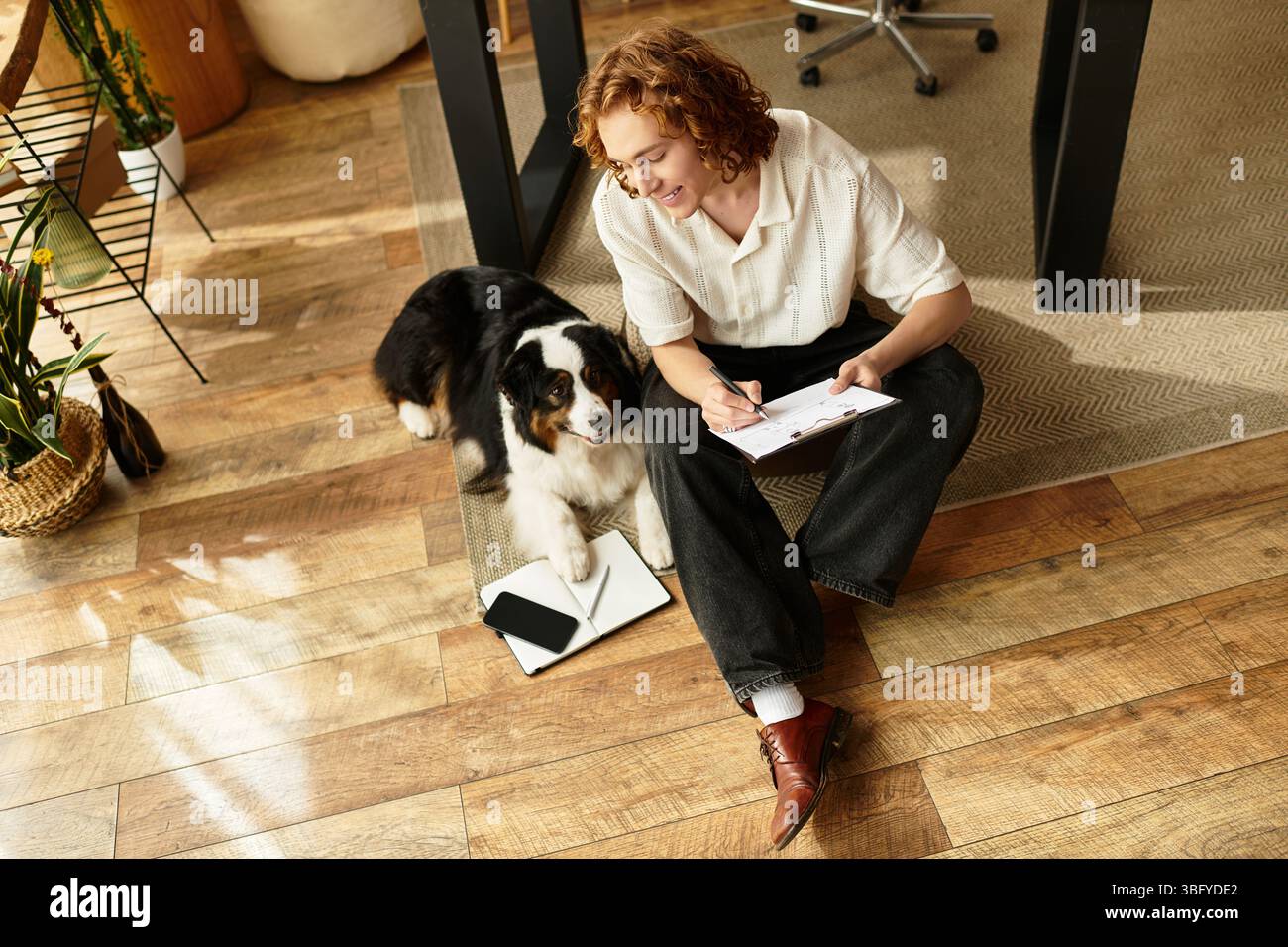 Il giovane si rilassa a casa, scrivendo appunti mentre il suo fedele cane rimane al suo fianco in una giornata di sole. Foto Stock