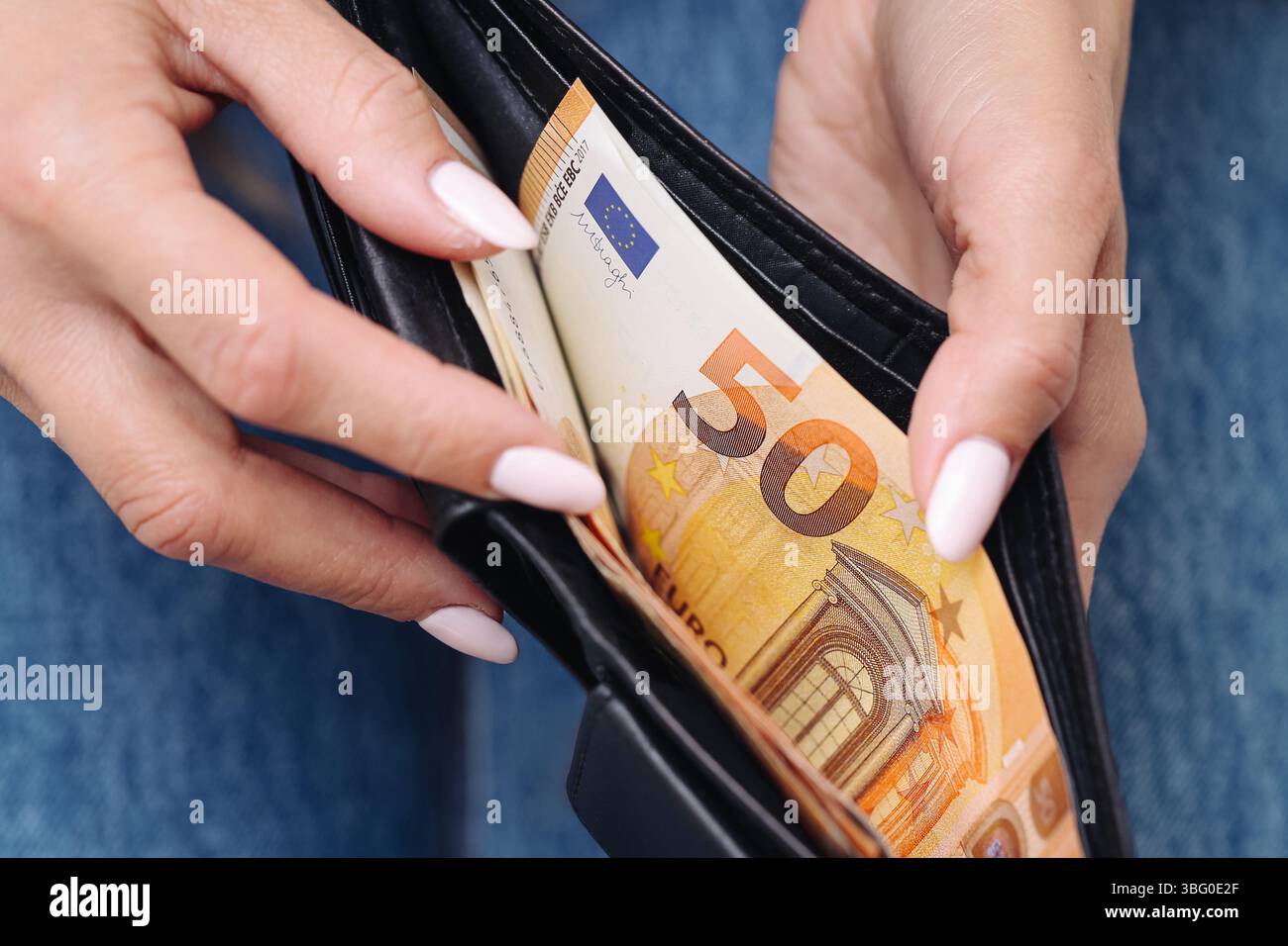 Portafogli con euro. Donna con manicure che mostra 50 euro. Concetto di finanza personale. Primo piano del portafoglio nero in pelle. Mani femminili e soldi. Foto Stock