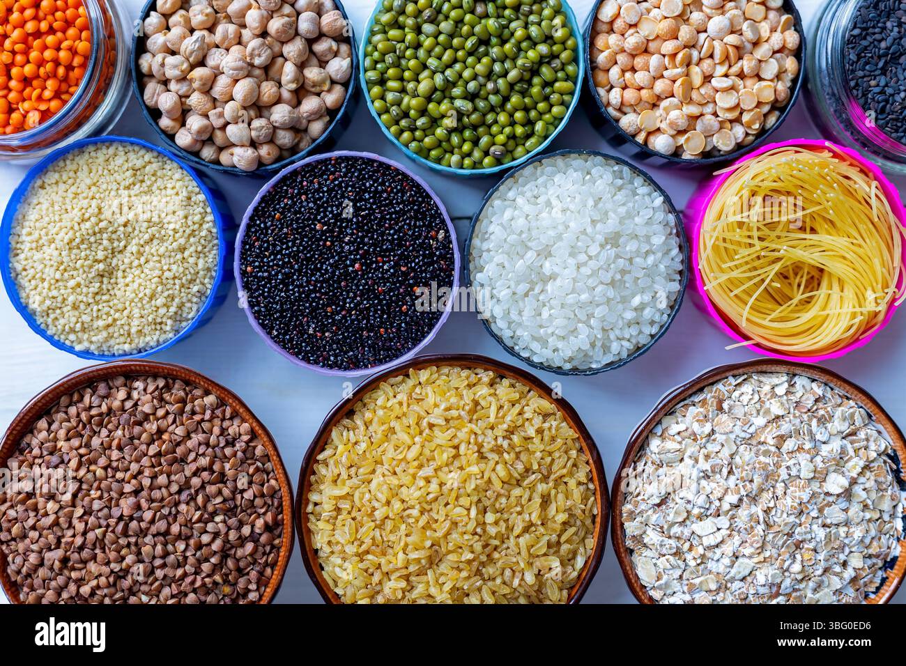 Cereali secchi assortiti, legumi e pasta in ciotole colorate. Vista dall'alto di vari tipi di cereali secchi, legumi e pasta disposti in ciotole colorate su un Foto Stock