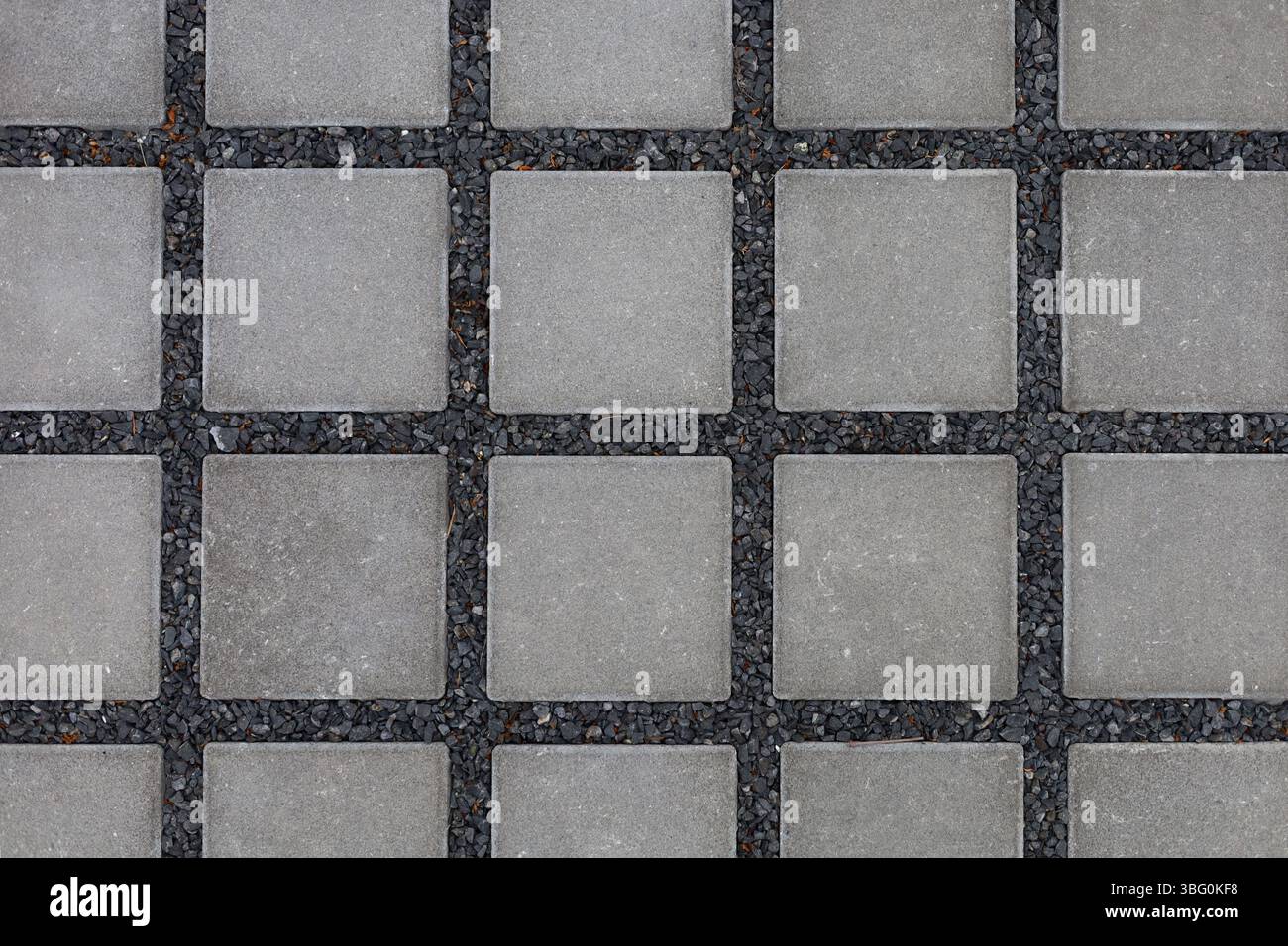 Mattonelle quadrate grigie su un substrato di piccole pietre nere Foto Stock