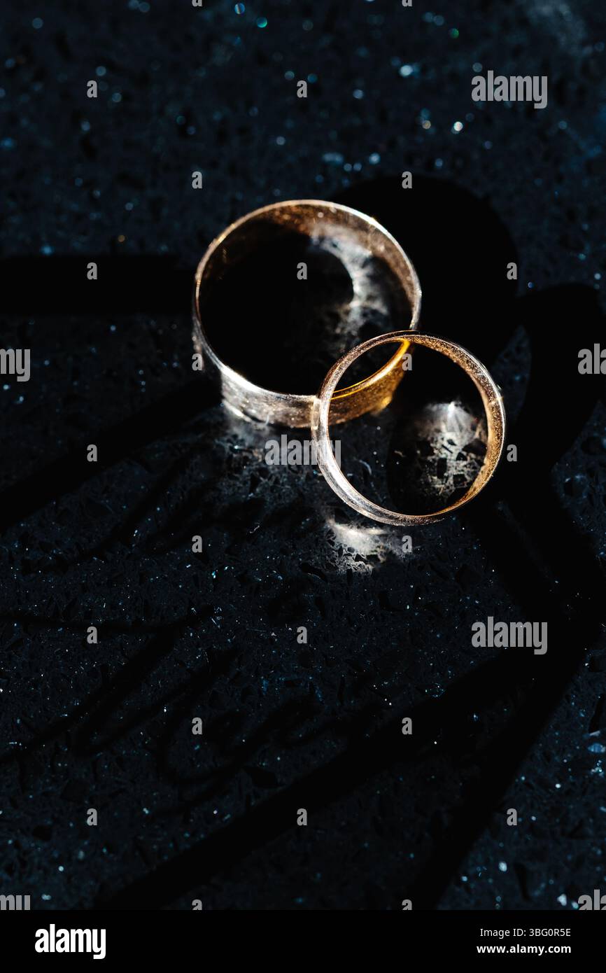 Due fedi nuziali che riflettono la luce sulla superficie di marmo scuro, che rappresentano impegno, amore e matrimonio Foto Stock