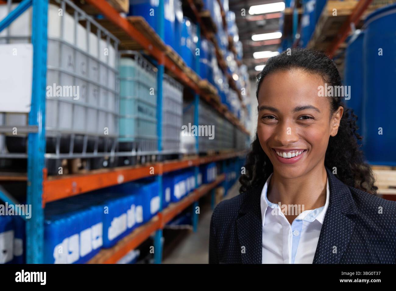 Corsia del magazzino industriale che si estende in lontananza, per contenere barili blu e contenitori IBC grigi Foto Stock