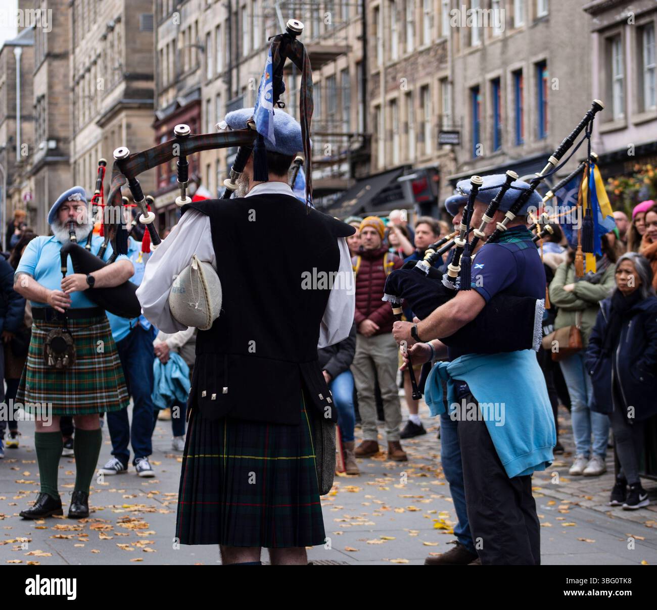 Uno spettacolo di strada con bagpiper scozzesi in tradizionali kilt circondati da un pubblico impegnato in un ambiente urbano. Il Royal Mile Edinburgh Foto Stock
