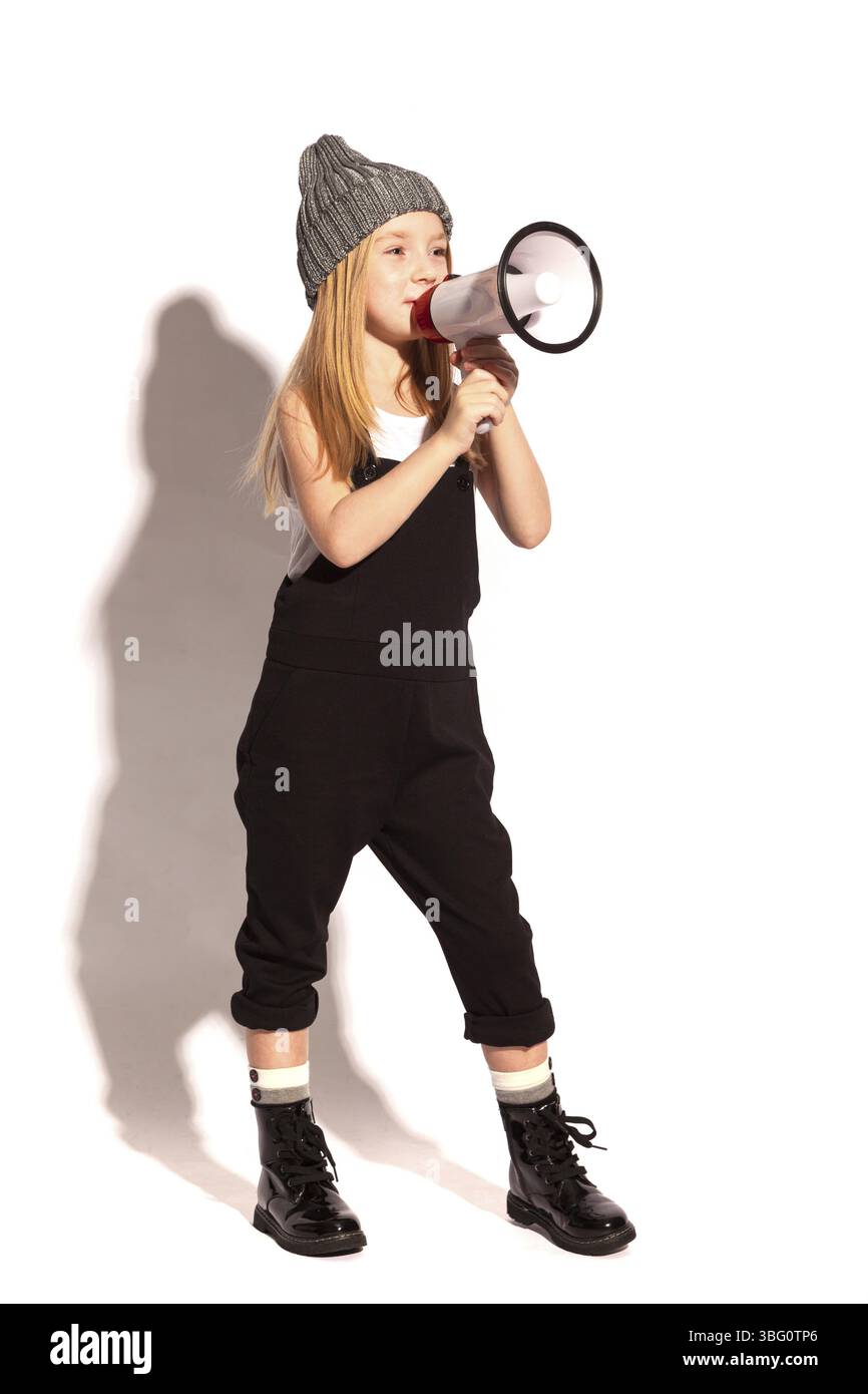 Isolata su una ragazza bianca dai capelli rossi, allegra e senza denti con tute nere, t-shirt bianca, cappello grigio e scarpe lacci laccate, che parla nella Foto Stock