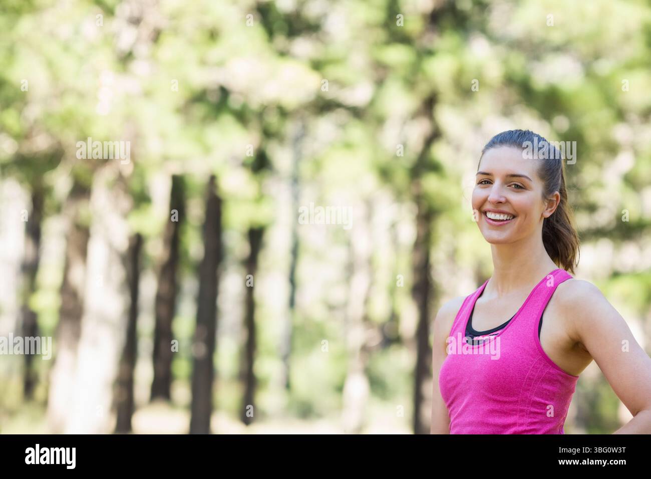 Donna appassionata di fitness in piedi sul sentiero della foresta illuminato dal sole con top rosa e reggiseno nero, spazio fotocopie Foto Stock