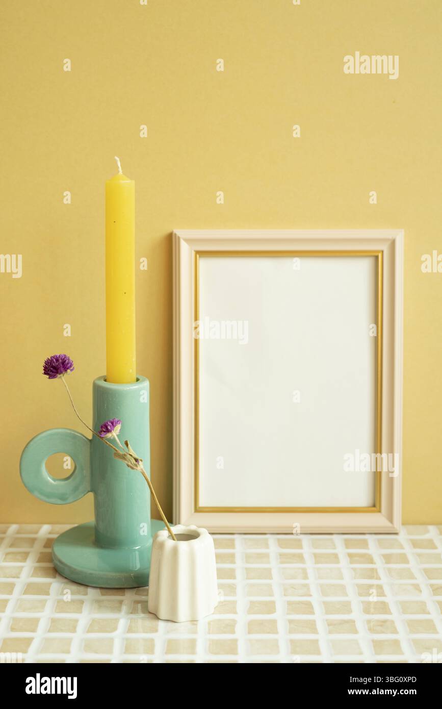 Cornice vuota e candela, fiore sul tavolo di tessere di controllo. sfondo giallo parete Foto Stock
