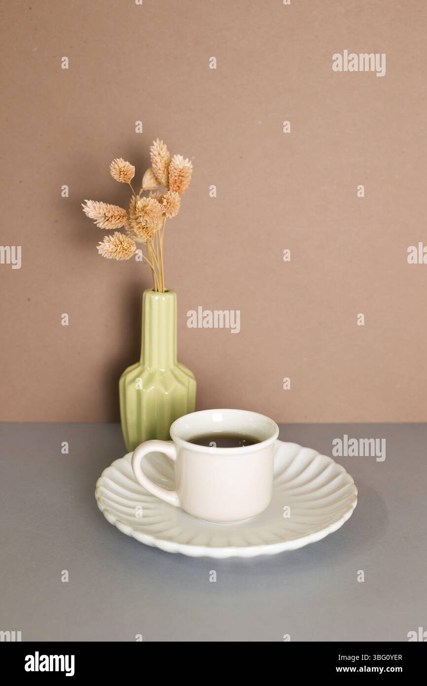 Tazza di tè e vaso di pianta secca rosa su tavola grigia. Parete di fondo marrone Foto Stock