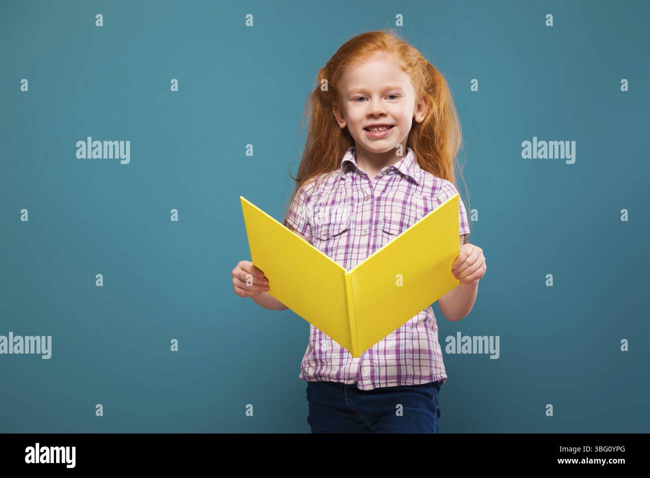 Isolata su un'attraente rossa caucasica di colore blu, con camicia a quadri bianca e jeans blu, con lunghi capelli arrugginiti, piegatrice di carta gialla, aperta a pieghe Foto Stock