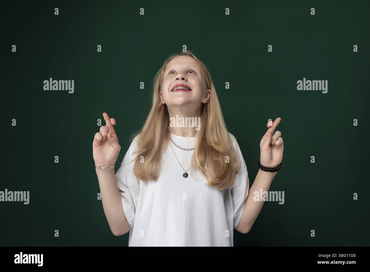 Donna in piedi davanti a una parete verde, che guarda direttamente la fotocamera. Sembra calma e composta nella sua postura Foto Stock