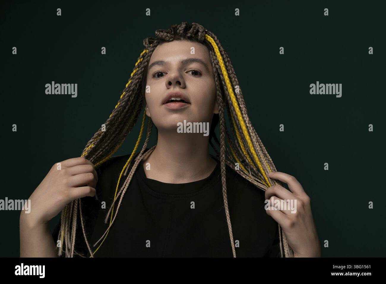Una donna con i dreadlock è in piedi in posizione verticale davanti a uno sfondo verde brillante. I suoi capelli sono modellati in lunghi e spessi dreadlock che le cadono a cascata Foto Stock