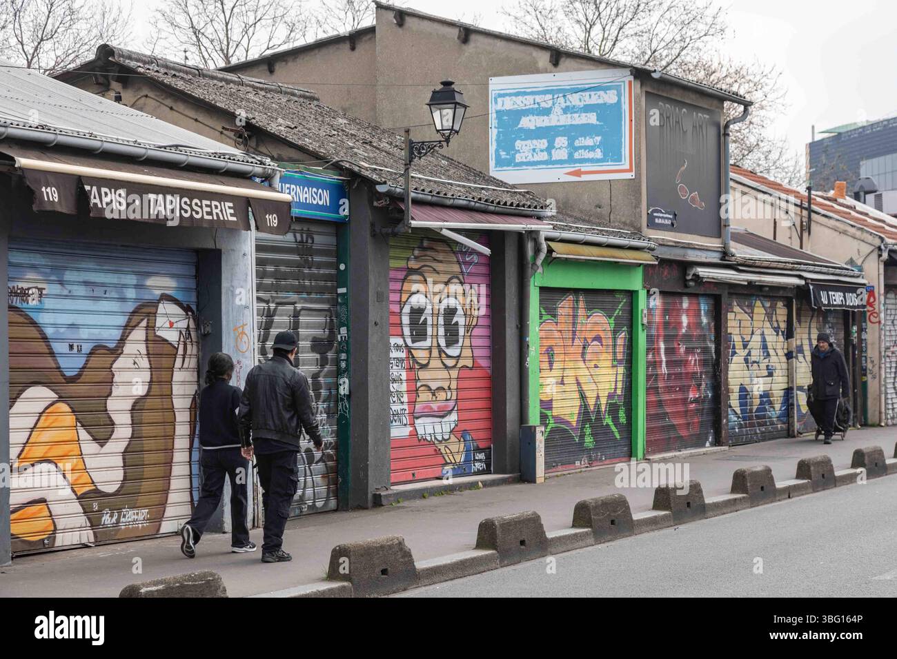 La coppia passeggia davanti alle porte arrotolate di antiquariato chiuso e ai negozi di seconda mano del Marché aux puces a Saint-Ouen-sur-Seine, Francia Foto Stock