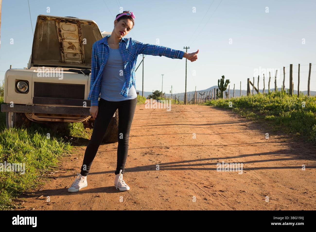 Donna che fa autostop accanto a un pick-up bianco con cofano aperto su una strada rurale sterrata, spazio fotocopie Foto Stock