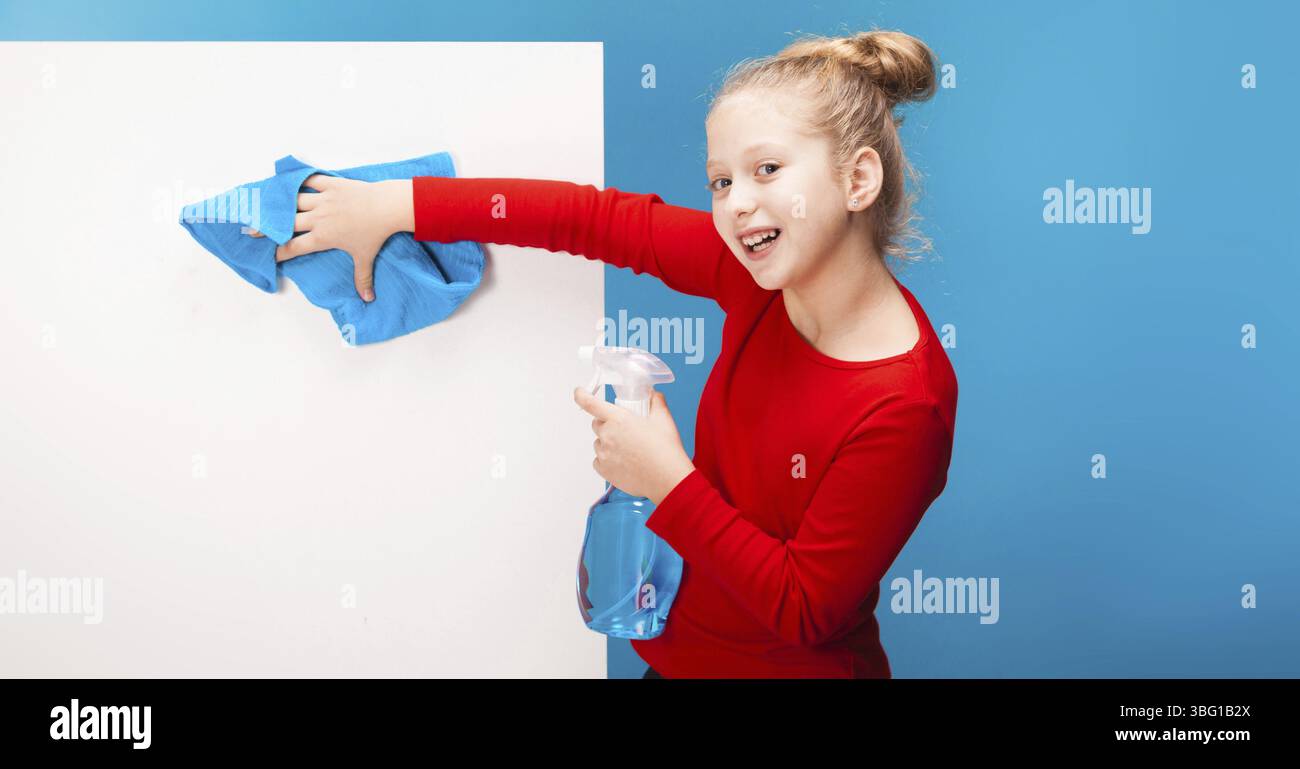 Isolata su una ragazza blu sorridente in pullover rosso con cappa dai capelli chiari, lucida il backgroung bianco con un panno blu e uno spray detergente. copyspace Foto Stock