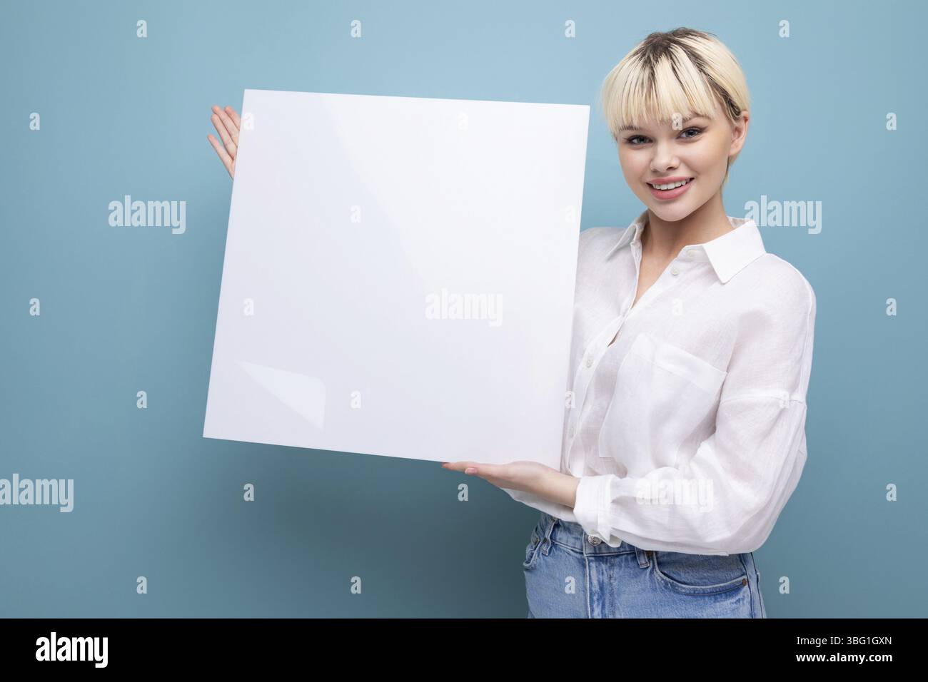 Giovane donna bionda di successo in ufficio con una camicia bianca e jeans tiene un pezzo di carta per inserire un annuncio pubblicitario. concetto di business Foto Stock