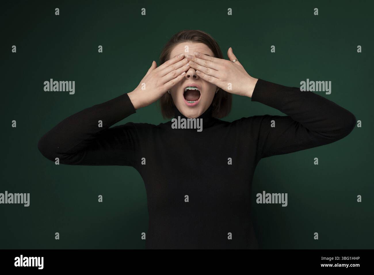 Una donna viene mostrata con le mani che coprono gli occhi. Sembra che stia proteggendo gli occhi da qualcosa di invisibile, forse usando il gesto per trasmettere fe Foto Stock