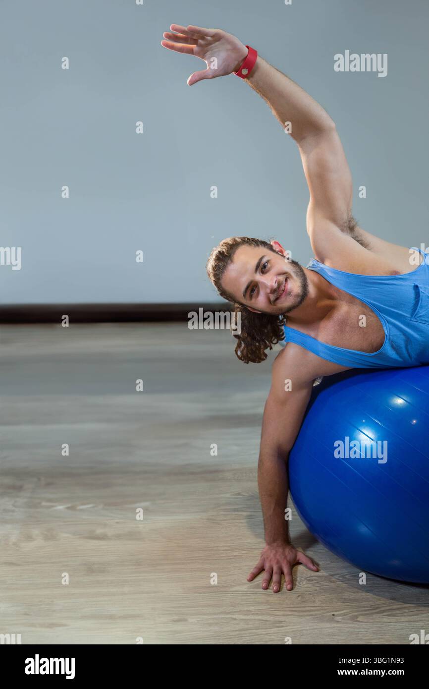 Uomo che si allunga con una palla stabilizzatrice blu in palestra con top atletico e spazio per copiare Foto Stock Uomo che si allunga con una palla stabilizzatrice blu in palestra con top atletico e spazio per copiare Foto Stock