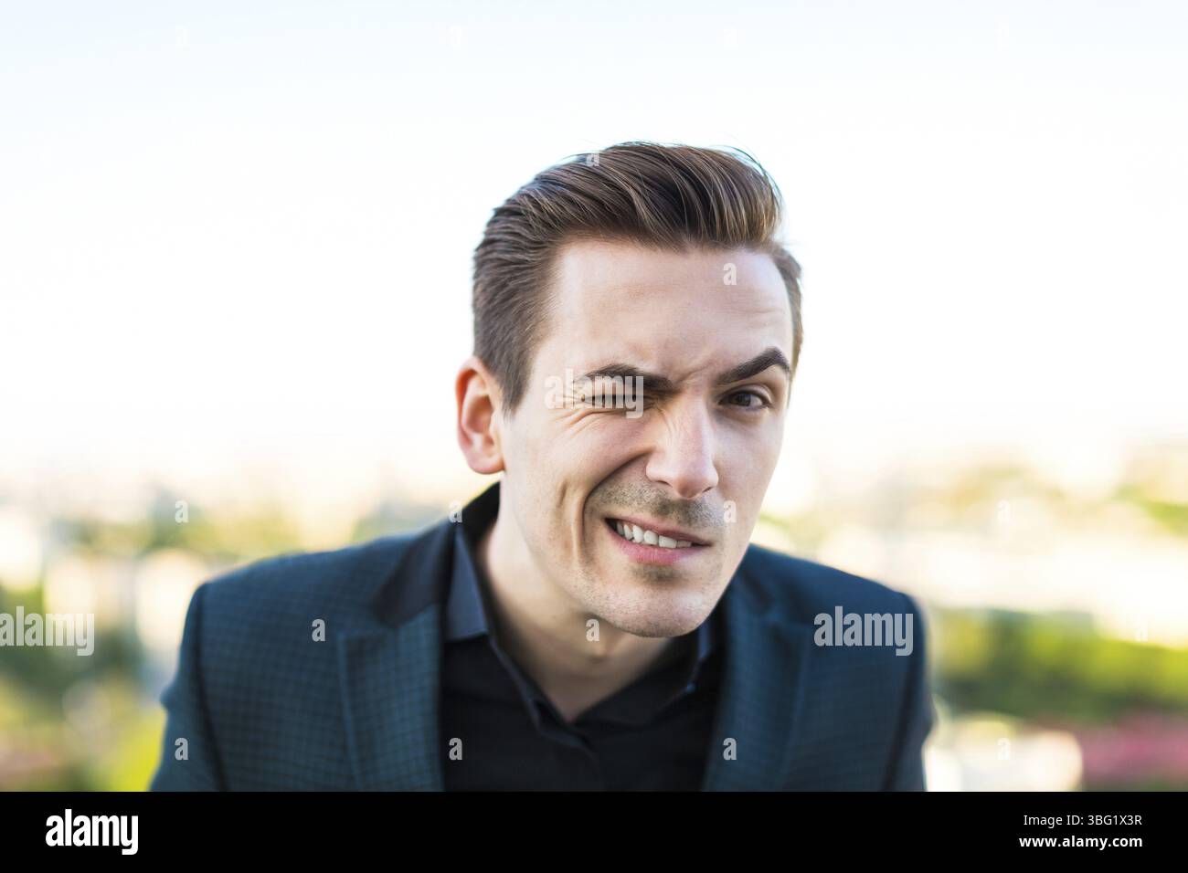 Uomo d'affari caucasico brunetta con tuta scura, camicia nera e costoso cavalletto per orologi sul tetto, guarda la fotocamera, rendendo i volti blured ci Foto Stock