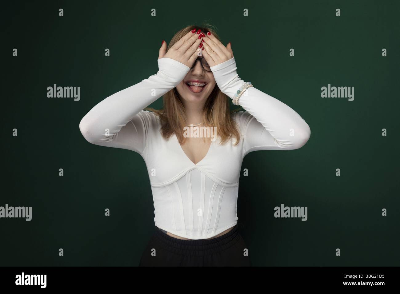 Si vede una donna che copre gli occhi con le mani. Il suo volto è parzialmente oscurato dalle sue mani, suggerendo un gesto di schermatura o di blocco di somet Foto Stock