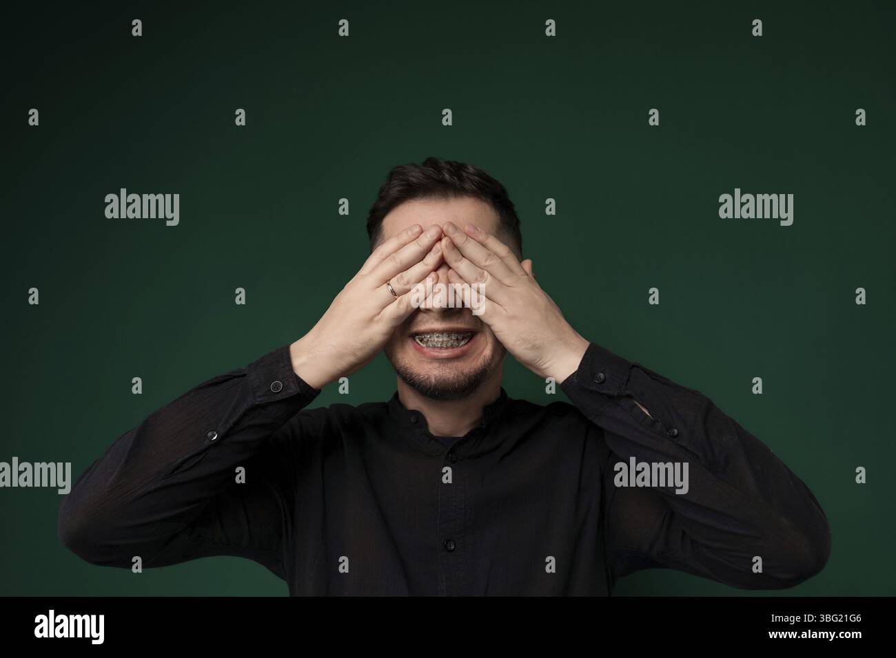 Un uomo viene mostrato con entrambe le mani che coprono gli occhi. Sembra che stia proteggendo gli occhi da qualcosa o esprimendo angoscia Foto Stock