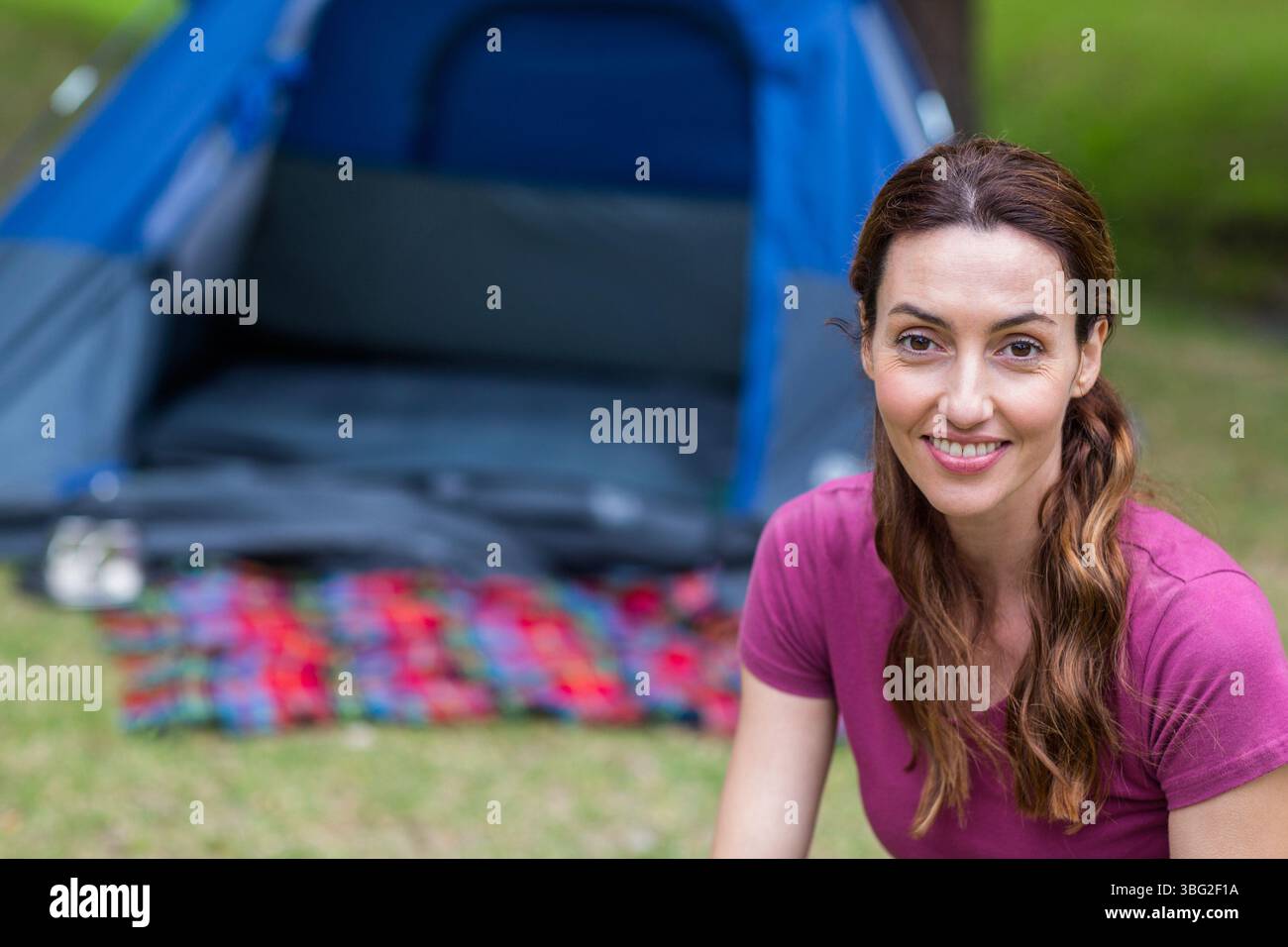 Donna seduta sull'erba di fronte alla tenda da campeggio blu su una coperta a quadri multicolore, spazio fotocopie Foto Stock