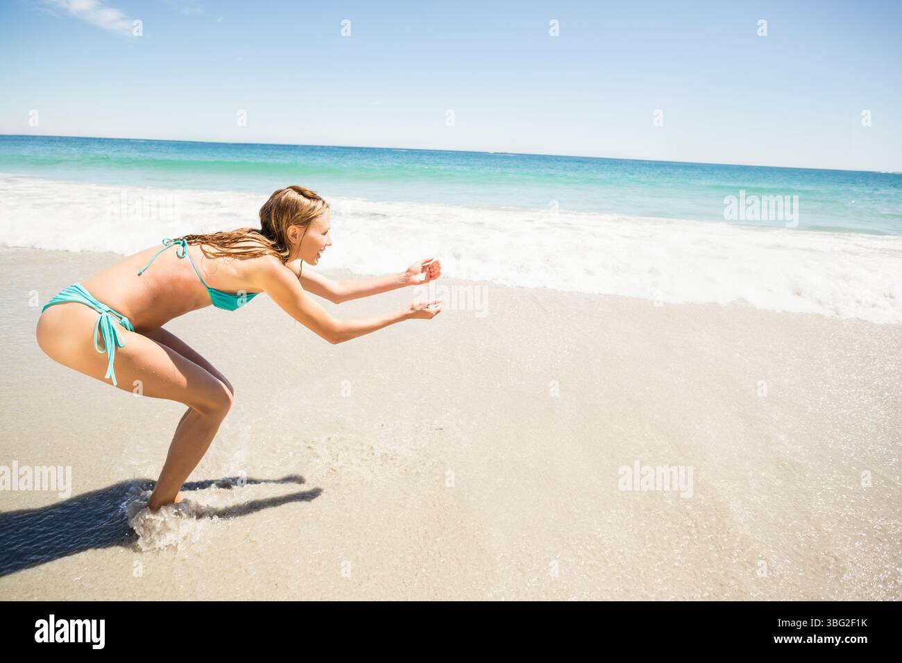 Le onde si infrangono sulla sabbia bagnata sotto il cielo azzurro e la luce del sole splende sulle acque turchesi Foto Stock