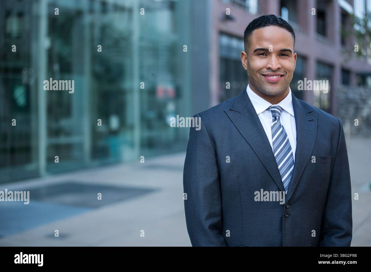 Uomo afroamericano in piedi su un passaggio pavimentato all'esterno di un moderno edificio per uffici in completo, copia spazio Foto Stock