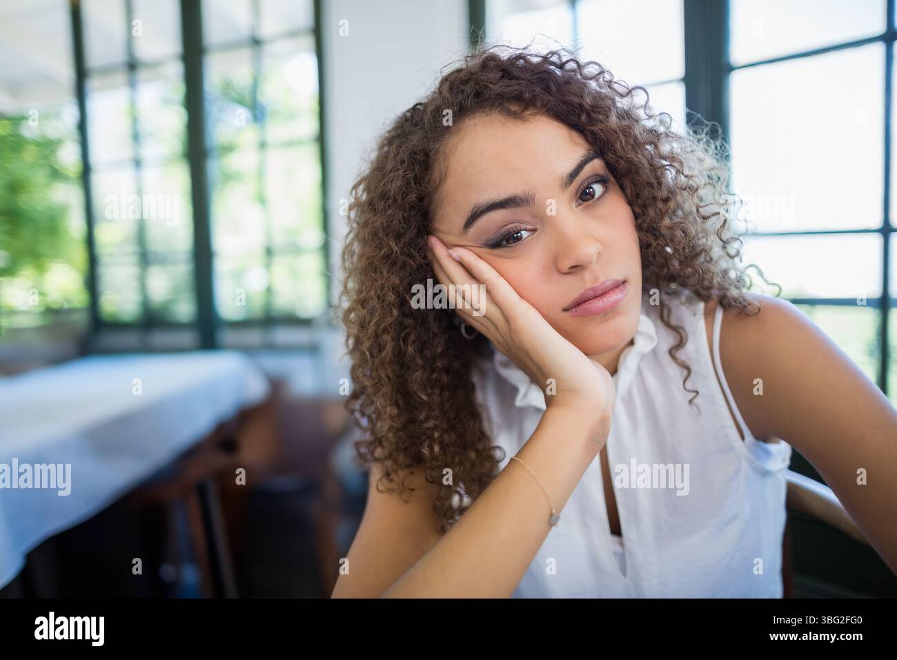 Donna che indossa un braccialetto, guarda davanti al tavolo di legno accanto alle finestre a griglia, copia spazio Foto Stock