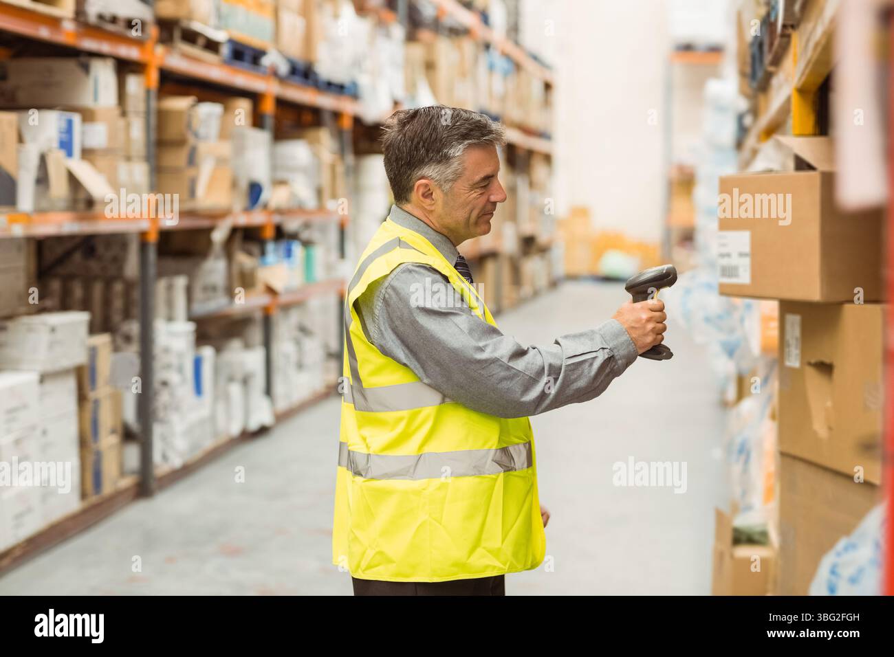 Lavoratore di magazzino che esegue la scansione di scatole di cartone su scaffali metallici nella corsia con scanner palmare Foto Stock