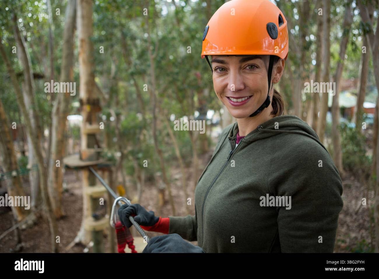 Donna che indossa un casco arancione che aggancia il cavo in acciaio sulla piattaforma del percorso di corda all'aperto, spazio per copiare Foto Stock