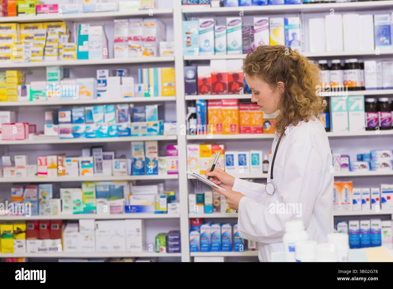 Scatole di farmaci e bottiglie che rivestono gli alti scaffali bianchi in farmacia al dettaglio sotto le luci del soffitto Foto Stock