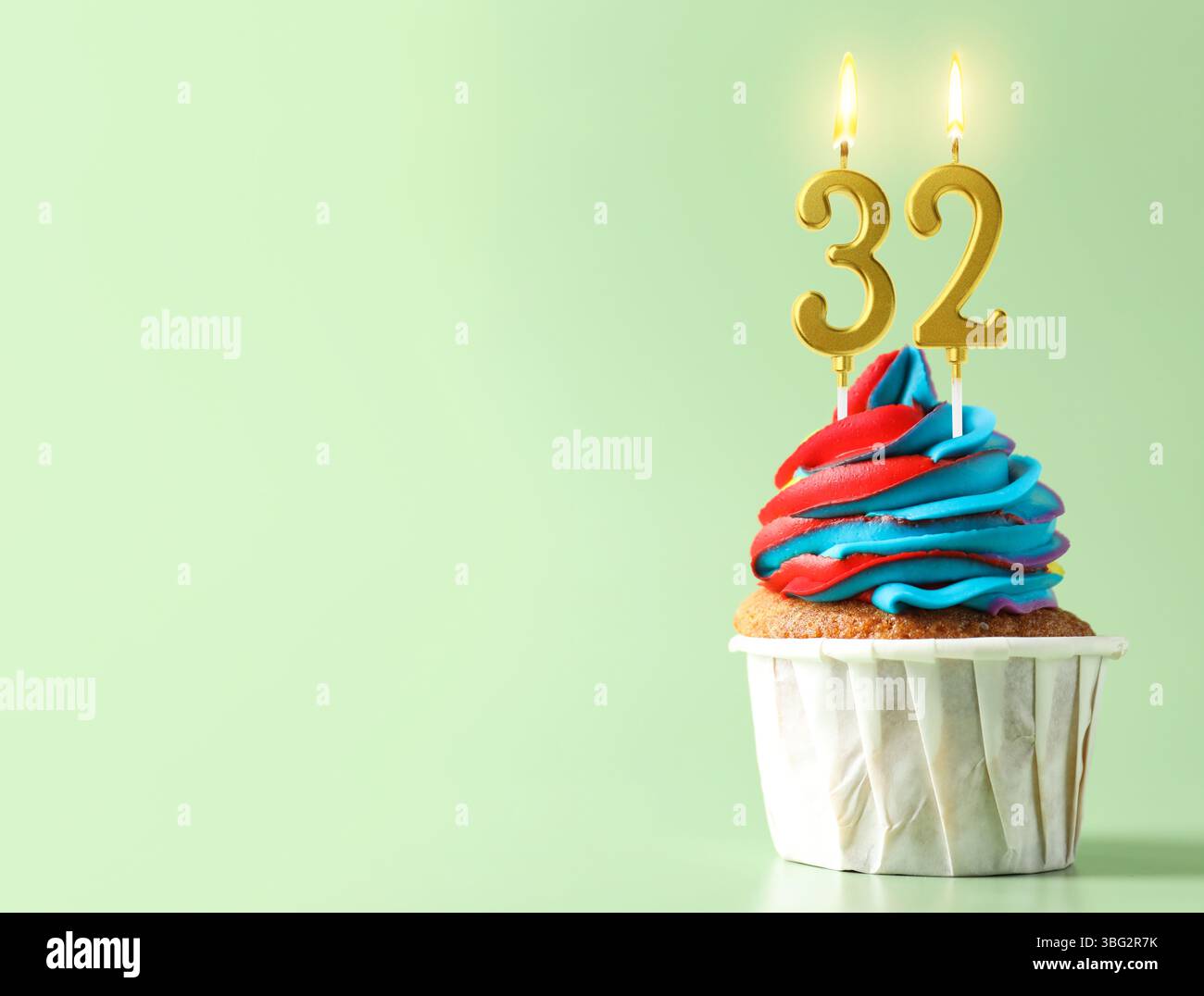 Delizioso cupcake con candele a forma di numeri accesi su sfondo turchese chiaro, spazio per il testo. 32° compleanno o altra occasione speciale Foto Stock