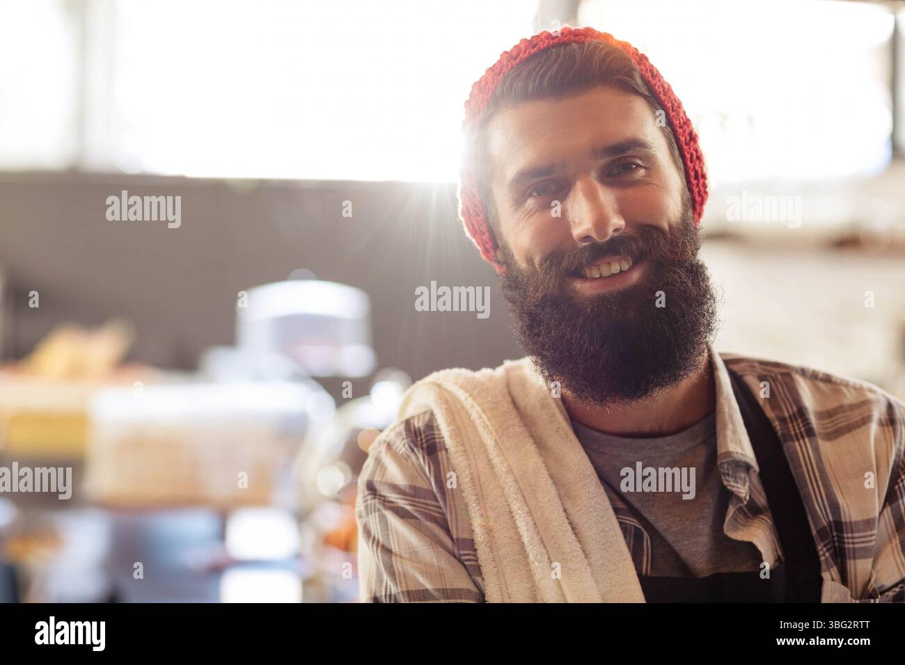 Barista maschile in piedi al bar con grembiule scuro, cappello rosso vicino ai pasticcini, spazio per le copie Foto Stock