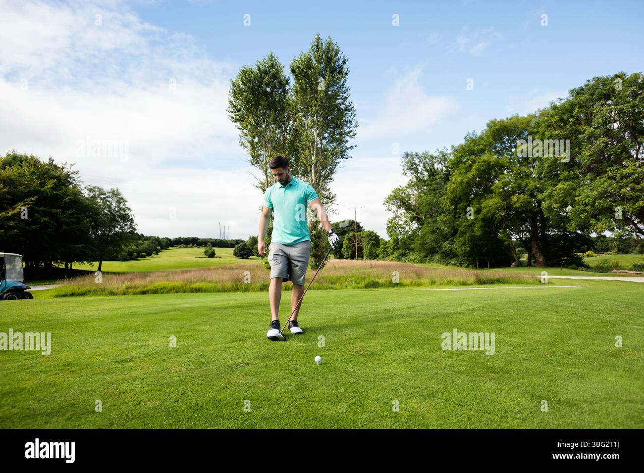 Golfista dilettante maschile che indossa guanti, tiene la mazza e mette la palla sul tee box del parco Foto Stock