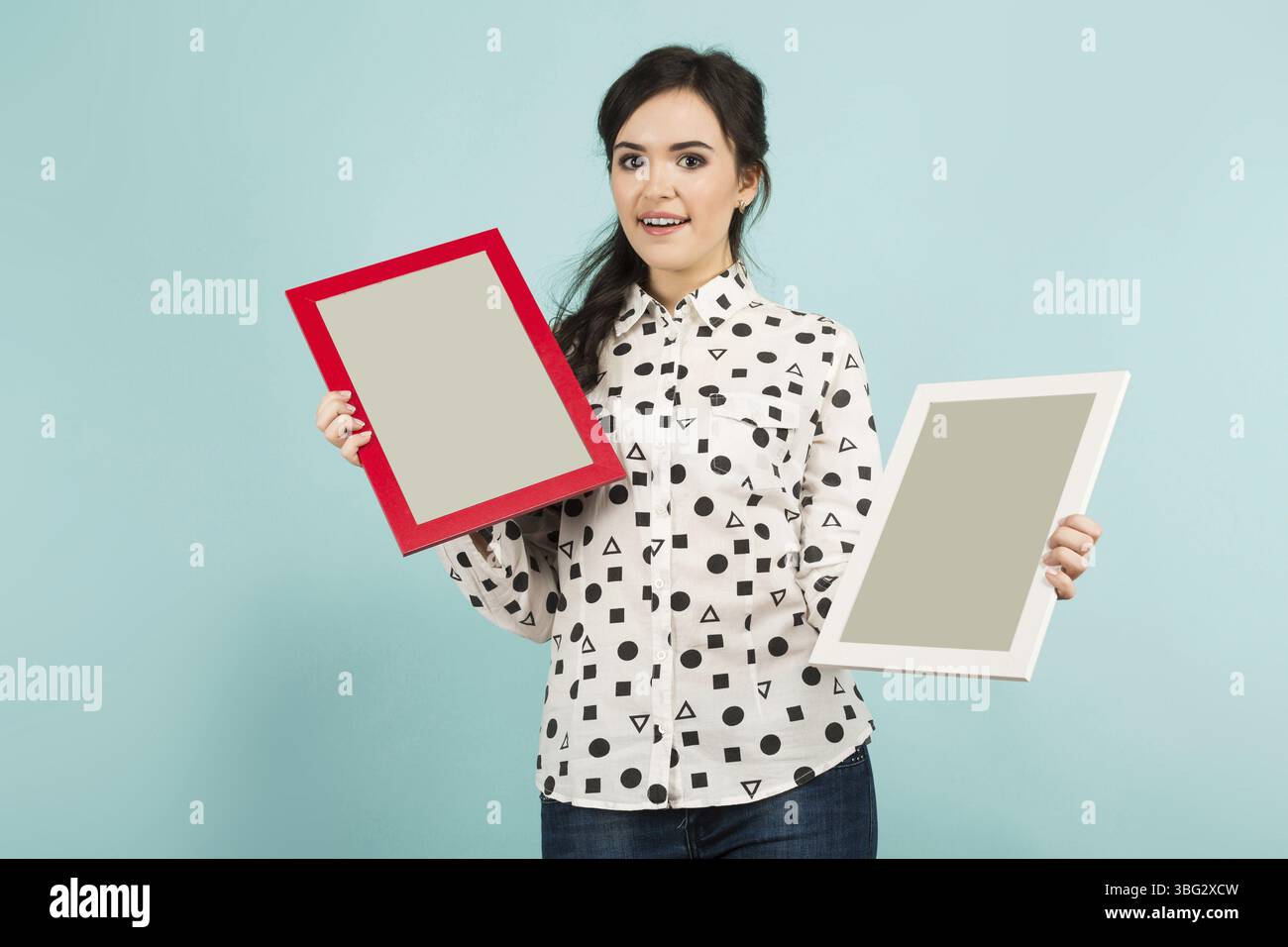 Ritratto di una giovane donna in camicia bianca e due cornici in posa su sfondo blu con copyspace Foto Stock