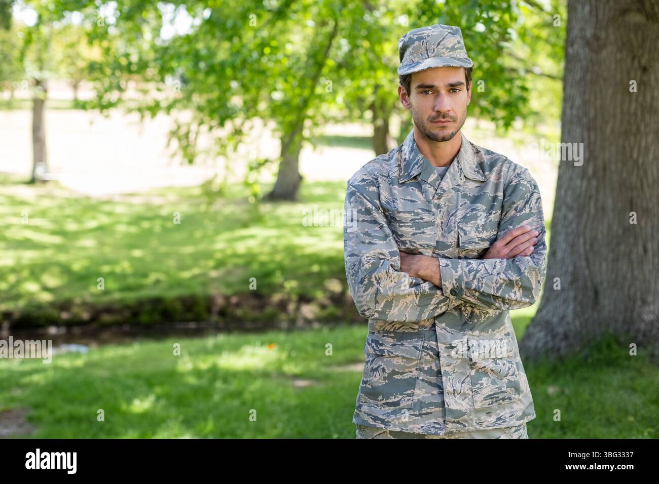 Soldato maschile che incrocia le armi nel parco in uniforme mimetica e cappello da albero, ruscello, copia spazio Foto Stock