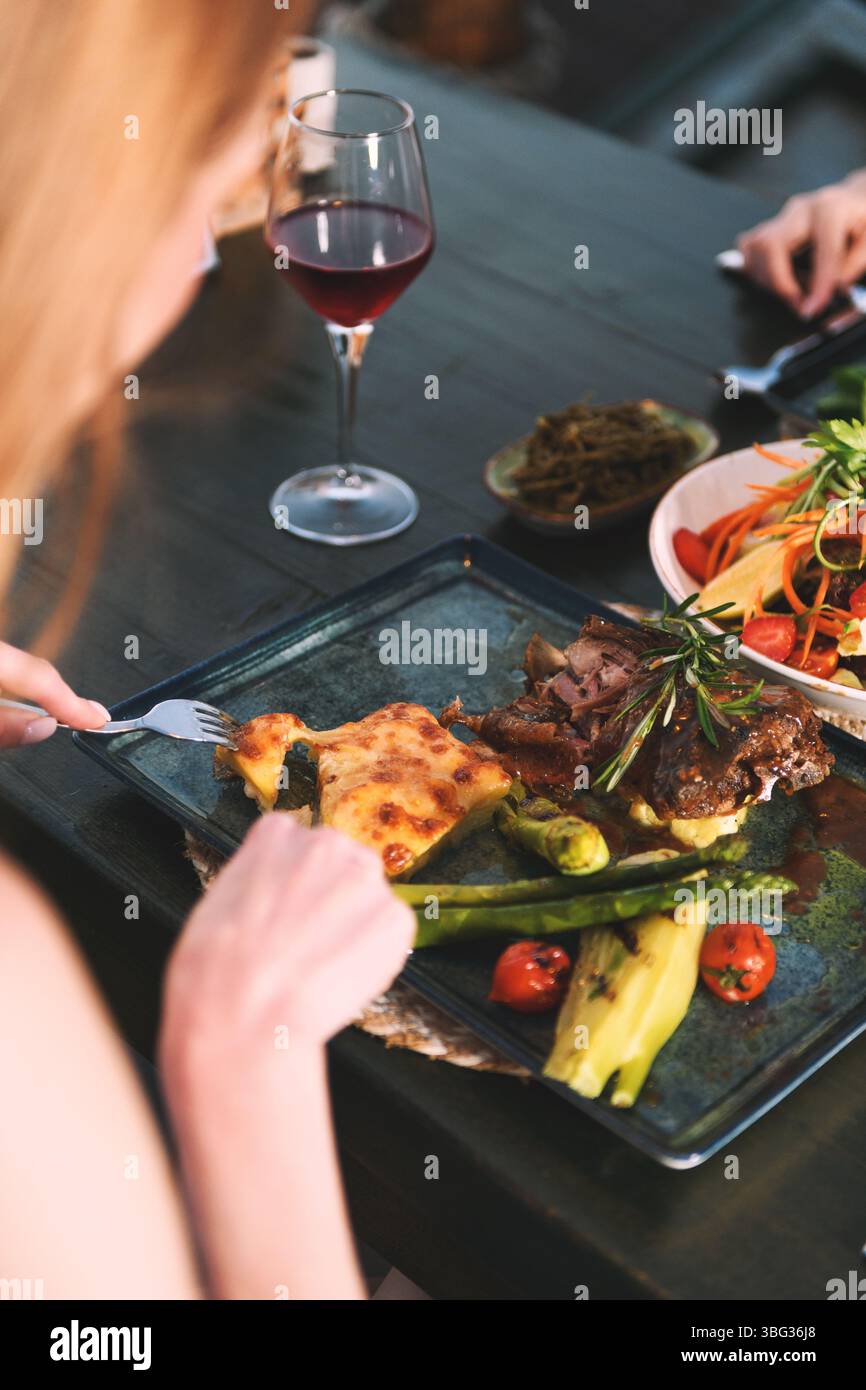 Uno scatto ravvicinato delle mani di una donna degli anni '20 che usa le posate per tagliarle in una bistecca in un ristorante di un hotel di lusso. Foto Stock